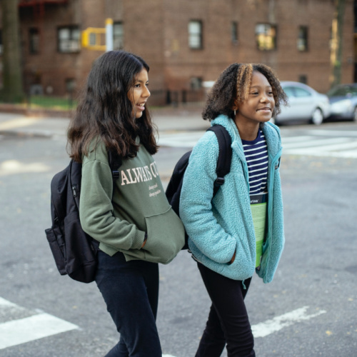 2 children in backpacks crossing a street while chatting